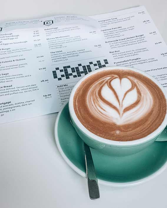 Flat white in a green ceramic cup with the menu for the cafe Crack Kitchen Adelaide