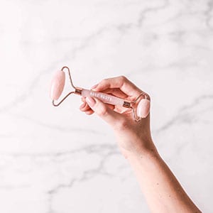 Pink quartz face roller in front of a marble Everyday Co backdrop